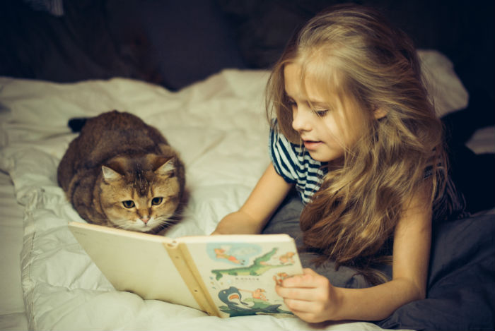 A girl holding a book and a cat